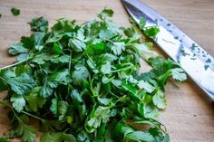 fresh cilantro on a cutting board with a knife next to the cut up parsley