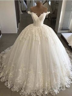 a white wedding dress with flowers on the skirt and off the shoulder, is displayed in front of a mirror