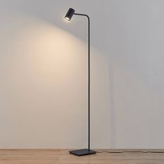 a black floor lamp with a white wall in the background and a wooden floor to the side