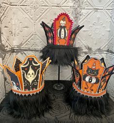 three halloween crowns with black feathers and cats on them are sitting on a table in front of a white wall