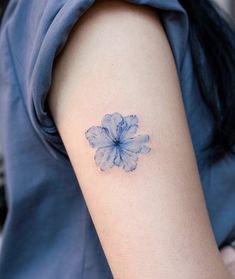 a small blue flower tattoo on the left upper half of the arm, and behind it is a light blue dress