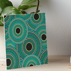 a blue and black art work with circles on it, sitting next to a potted plant