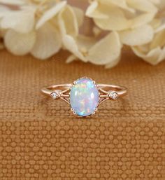 a white opal and diamond ring sitting on top of a brown cloth next to flowers