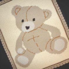 a crocheted teddy bear is sitting on the floor next to a white blanket