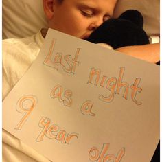 a young boy sleeping in bed holding a sign that says last night as a year old