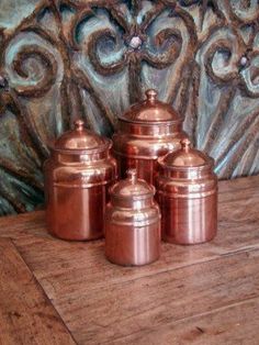 three copper canisters sitting on top of a wooden table next to a wall