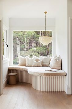 a large window seat with pillows on it in front of a white wall and wooden floor