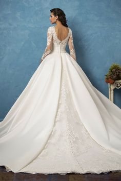 a woman in a white wedding dress is standing against a blue wall with her back to the camera