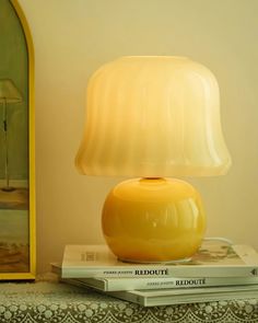 a yellow lamp sitting on top of a stack of books next to a framed painting