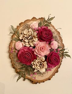 a bunch of flowers that are on top of a wooden slice with leaves and pine cones