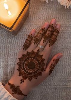 a woman's hand with henna on it next to a candle and flowers