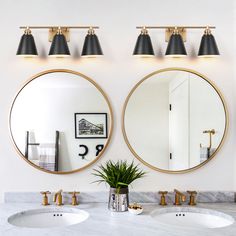 two round mirrors hanging on the wall above sinks in a white bathroom with gold trim