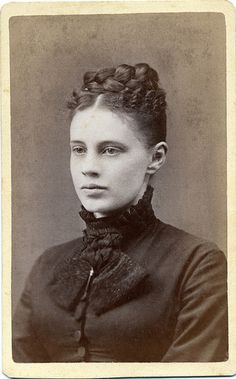 an old black and white photo of a woman with braids on her hair, wearing a dress