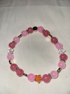 a pink beaded bracelet with an orange star charm on it's end and a gold plated clasp