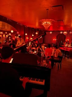 a group of people sitting around a piano in a room with red lighting and chandeliers