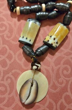 This artfully deamatic necklace consists of black, yellow and off white beads. Black hand rolled and painted beads adorn a black cord, along with yellow, black and off white ceramic beads. Also included are off white, and brass spacer beads.The focal is off white with a Cori Shell. It closes with a brass toggle clasp Black Artisan Necklaces For Beach, Black Artisan Necklace For Beach, Artisan Black Necklace For Beach, Adjustable Yellow Necklaces With Wooden Beads, Adjustable Yellow Necklace With Wooden Beads, Adjustable Yellow Wooden Beads Necklace, Black Wooden Beads Necklace For Beach, Handmade Black Shell Necklace In Bohemian Style, Handmade Black Bohemian Shell Necklace