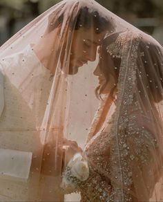 the bride and groom are looking at each other while they stand under their veils