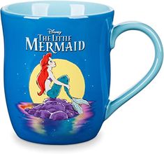 the little mermaid coffee mug is blue and has an image of ariel sitting on a rock