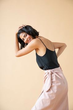 a woman in a black top and pink skirt poses for the camera with her hand on her head