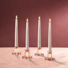 three candles are lined up in the same row on a pink surface with gold accents