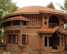 a round brick building with red tile on the roof and windows, surrounded by palm trees