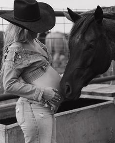 a black and white photo of a woman in cowboy hats petting a horse