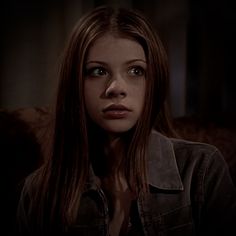 a woman with long hair sitting on a couch in a dark room looking at the camera