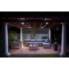 an outdoor living area with couches, tables and lights on the patio at night