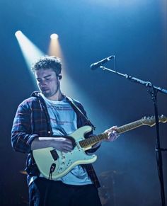 a man standing in front of a microphone while playing an electric guitar