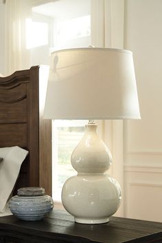 a white lamp sitting on top of a table next to a bed in a bedroom