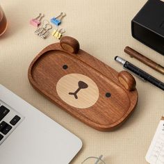 a desk with a laptop, pen and bear shaped wooden case on it's side