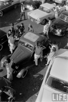 an old black and white photo of people standing around cars