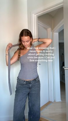 a woman in jeans and tank top pulling on a tie with her hands while standing against a wall