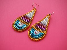 a pair of beaded earrings sitting on top of a pink surface