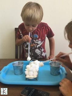 two young boys sitting at a table making marshmallows