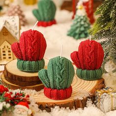 two knitted cactus candles sitting on top of a wooden log in front of christmas decorations