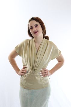 Love this pretty, goes with anything earth-tone blouse! Simply yelps 30's-40's glamour to me! Pair with a simple wool skirt or modernize it with some dark wash jeans! So flattering and unique! features *hidden button closure at the front *cut buttons at the booty! *elegant loose fit *pale gold color *fitted at hips for a drop waist look *shiny/silky material In great vintage condition, no major flaws Model is 5'10, 152lbs and wears size 8/10. Fit was great, slightly snug in the hips material is Retro Beige V-neck Top, Vintage V-neck Blouse For Evening, Retro V-neck Blouse For Party, Fitted Retro Beige Blouse, Vintage Beige V-neck Top, Fitted Vintage V-neck Blouse, Fitted Vintage Beige Top, Vintage Beige Blouse For Party, Vintage Cream V-neck Top