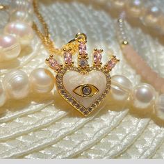 "Heart Evil Eye Necklace with Crown and Pink Stones.  Introducing our stunning 18k gold filled Crown Evil Eye Heart Necklace, a one-of-a-kind piece of jewelry that is sure to turn heads. Crafted from high-quality materials, this necklace features a beautifully intricate crown design, adorned with sparkling cubic zirconia stones, that sits atop a striking heart-shaped evil eye pendant. The pendant is carefully handcrafted with a beautiful emerald pink stone, a powerful symbol of protection and good fortune. Made with 18k gold filled chain that is both durable and resistant to tarnishing, this necklace is perfect for everyday wear and will last you for years to come. Whether you're looking to add a touch of elegance to your work outfit or to make a statement on a night out, this necklace is Handmade Rose Gold Heart Pendant Jewelry, Dainty Heart Beads Pendant Jewelry, Delicate Gold Plated Heart Jewelry, Handmade Gold Plated Jewelry For Valentine's Day, Delicate Heart-shaped Gold Plated Jewelry, Handmade Heart-shaped Gold Plated Jewelry, Gold Plated Charm Necklaces With Heart Beads For Gift, Heart Beads Cubic Zirconia Jewelry For Gifts, Gold Plated Heart Beads Charm Necklace For Gift