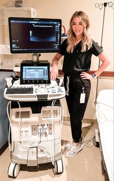 a woman standing next to a laptop computer on top of a hospital bed in front of a monitor