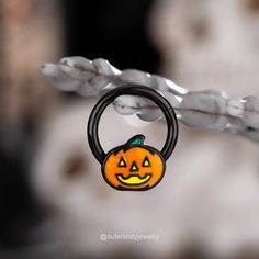 a close up of a pumpkin shaped ring on a piece of wire with an evil face painted on it