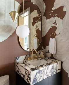 a bathroom with a marble sink and gold accents on the wall, along with a round mirror