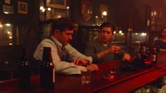 three men sitting at a bar with bottles and glasses