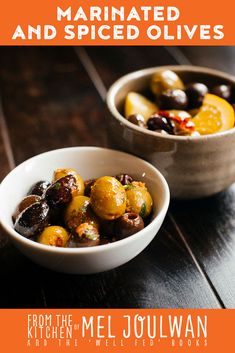 two white bowls filled with olives and other vegetables on top of a wooden table