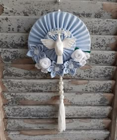 a blue fan with flowers and a bird hanging from it's side on a wall