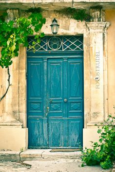 an old building with a blue door and green vines growing on the outside, in front of it