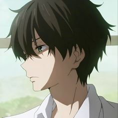 a man with black hair and green eyes stares into the distance while standing in front of a window