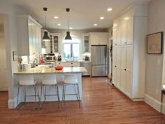 a large kitchen with white cabinets and wood flooring is seen in this image, there are four stools at the center of the island