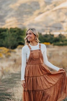 Step out in style with THE EMILIE LACE SKIRTALL IN RUST. This overall dress is sure to bring you plenty of compliments with its rust hue, chic lace detailing, and chiffon contrast panel. Don't forget to twirl in this one-of-a-kind midi overall dress! Paired with THE LAYERING CAP SLEEVE TEE IN WHITE BY MIKAROSE and THE FLORANCE FLORAL MESH LAYERING LONG SLEEVE IN BIEGE Embroidered lace details Midi length Chiffon contrast panel Tiered Self: 100% cotton, Contrast: 100% polyester, Lining: 100% rayo Heartland Outfits, Long Sleeve Shirt Under Dress, Overall Dress Outfit Fall, Fall Senior Pics Outfits, Western Dress Outfits, Layered Dress Outfit, Mesh Layering, Layering Long Sleeve, Overall Dress Outfit