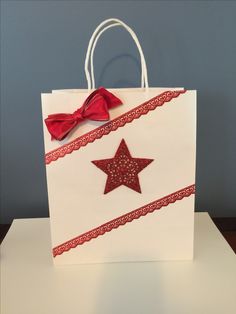 a white shopping bag with a red star on it and a ribbon tied around the handle