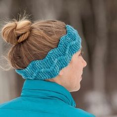 a woman wearing a blue headband in the winter with snow on the ground and trees behind her